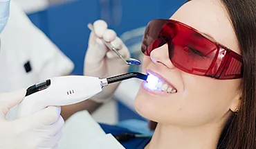 Patientin mit Schutzbrille während einer Zahnaufhellung mit Bleaching-Gerät. Moderne ästhetische Zahnmedizin für schöne Zähne in Lübeck.